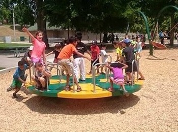 A group of happy children playing on a green and yellow merry-go-round during a fun and safe March break camp for kids in Burlington.