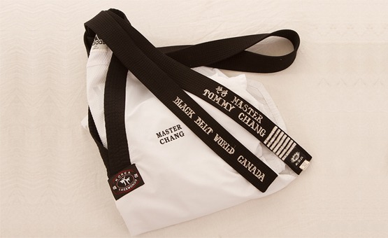 A folded white Taekwondo uniform and a black belt embroidered with "Master Tommy Chang" and "Black Belt World Canada."